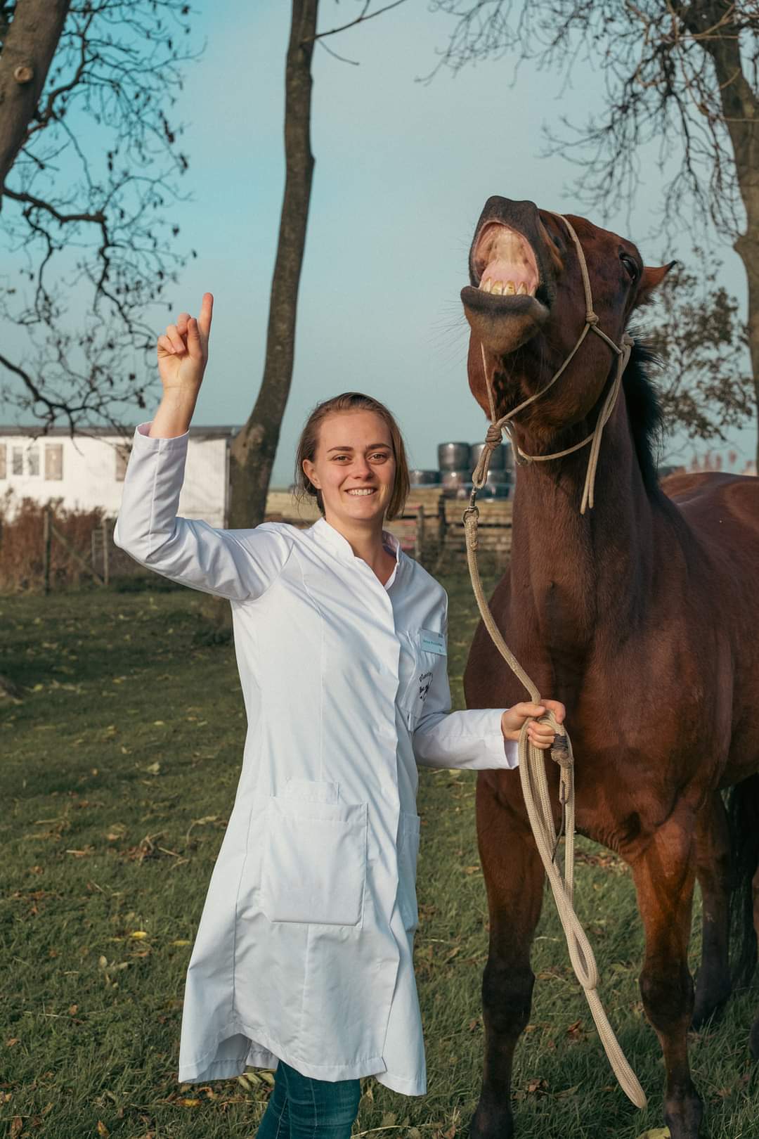 Donna in labjas met een paard op het erf